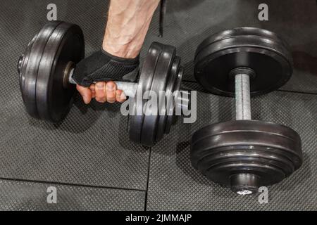 Zwei Kurzhanteln auf dem Boden des Fitnessraums, eine davon in der hand von mans Stockfoto
