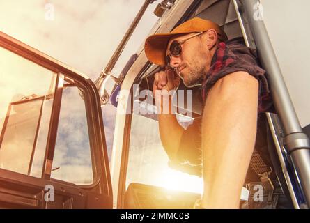 Nahaufnahme eines zufriedenen Lkw-Fahrers im Western Style Outfit, der nach erfolgreicher Lieferung aus seinem amerikanischen Lastwagen aussteigen konnte. Transport I Stockfoto