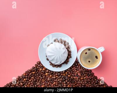 Weiße Tasse mit heißem Kaffee, Kaffeebohnen und Marschmalchen auf einem rosa Hintergrund. Stockfoto