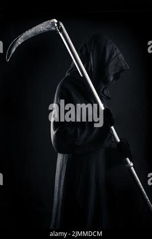Tod hält eine alte Sense scharfe Klinge auf den Schultern des Todes in der Dunkelheit Angst Stockfoto