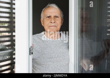 Einsamer älterer Mann, der in das Fenster schaut Stockfoto