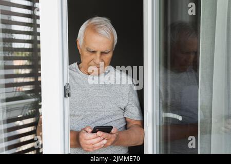 Älterer Mann mit Smartphone zu Hause Stockfoto