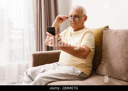 Ein älterer Mann mit Brille verwendet ein Smartphone Stockfoto