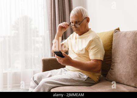 Ein älterer Mann mit Brille verwendet ein Smartphone Stockfoto