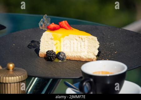 Köstlicher frischer Käsekuchen mit Beeren und eine Tasse Kaffee auf einem Tisch in einem Straßenrestaurant Stockfoto