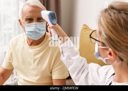 Arzt überprüft die Körpertemperatur bei einem älteren Mann während des Hausbesuchs Stockfoto