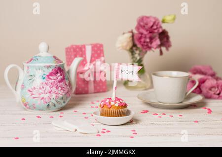 Köstlicher Kuchen mit dekorativer Flagge mit Mama Titel in der Nähe Teekannen Blumen Tasse Stockfoto