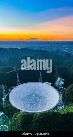 (220806) -- GUIZHOU, 6. August 2022 (Xinhua) -- Luftfoto vom 21. Juli 2022 zeigt eine Ansicht des fünfhundert Meter langen Aperture Spherical Radio Telescope (FAST), das bei Sonnenuntergang in der südwestlichen Provinz Guizhou in Betrieb ist. Das Hotel befindet sich in einer natürlich tiefen und runden Karstniederlage in der südwestlichen chinesischen Provinz Guizhou und begann IM Januar 2020 MIT der offiziellen Operation und wurde am 31. März 2021 offiziell der Welt eröffnet. Es wird angenommen, dass es das empfindlichste Radioteleskop der Welt ist. Mit FAST haben Wissenschaftler über 660 neue Pulsare identifiziert. (Xinhua/Ou Dongqu) Stockfoto