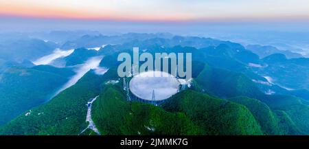 (220806) -- GUIZHOU, 6. August 2022 (Xinhua) -- Luftfoto vom 22. Juli 2022 zeigt Chinas fünfhundert Meter langes Aperture Spherical Radio Telescope (FAST), das am frühen Morgen in der südwestlichen Provinz Guizhou gewartet wird. Das Hotel befindet sich in einer natürlich tiefen und runden Karstniederlage in der südwestlichen chinesischen Provinz Guizhou und begann IM Januar 2020 MIT der offiziellen Operation und wurde am 31. März 2021 offiziell der Welt eröffnet. Es wird angenommen, dass es das empfindlichste Radioteleskop der Welt ist. Mit FAST haben Wissenschaftler über 660 neue Pulsare identifiziert. (Xinhua/Ou Dongqu) Stockfoto