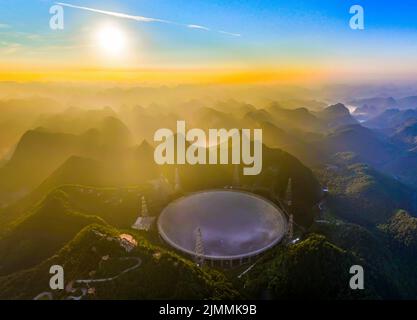 (220806) -- GUIZHOU, 6. August 2022 (Xinhua) -- Luftfoto vom 25. Juli 2022 zeigt Chinas fünfhundert Meter langes Aperture Spherical Radio Telescope (FAST), das bei Sonnenaufgang in der südwestlichen Provinz Guizhou in Betrieb ist. Das Hotel befindet sich in einer natürlich tiefen und runden Karstniederlage in der südwestlichen chinesischen Provinz Guizhou und begann IM Januar 2020 MIT der offiziellen Operation und wurde am 31. März 2021 offiziell der Welt eröffnet. Es wird angenommen, dass es das empfindlichste Radioteleskop der Welt ist. Mit FAST haben Wissenschaftler über 660 neue Pulsare identifiziert. (Xinhua/Ou Dongqu) Stockfoto