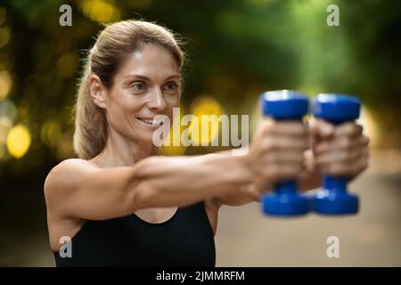 Nahaufnahme der motivierten sportlichen Frau beim Training mit Kurzhanteln im Park Stockfoto