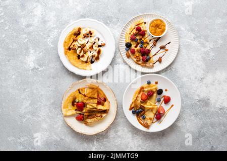 Teller mit Frühstückscrepes mit Beeren und Bananen auf heller Oberfläche Stockfoto