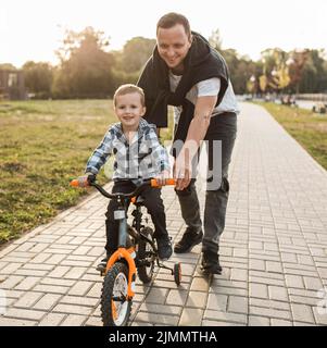 Vater hilft seinem Sohn beim Fahrradfahren Stockfoto
