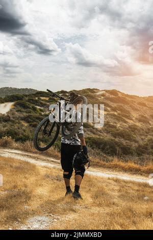 Professioneller Downhillfahrer, der sein Fahrrad auf der Schulter trägt Stockfoto