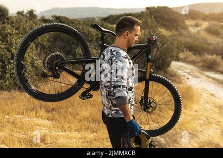 Professioneller Downhillfahrer, der sein Fahrrad auf der Schulter trägt Stockfoto