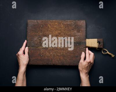 Leeres Holzschneidebrett in weiblichen Händen auf schwarzem Holztisch, Draufsicht Stockfoto