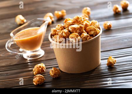 Karamellisiertes Popcorn in Papiereimer auf Holztisch Stockfoto