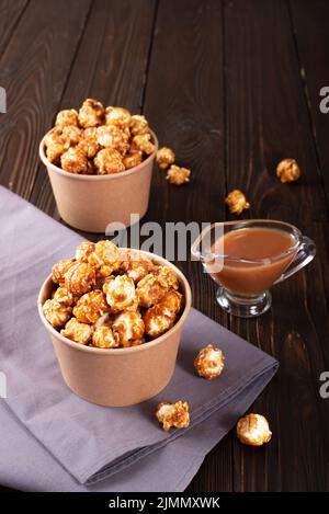 Karamellisiertes Popcorn in Papiereimer auf Holztisch Stockfoto