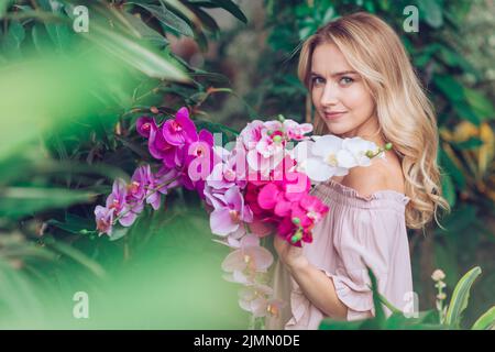 Blonde junge Frau steht Garten hält Orchidee Stockfoto