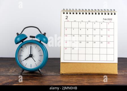 Kalenderdatum Februar 2022. Einfacher Sitzkalender Februar 2022 mit blauem Wecker auf dem Tisch. Effizienz und produktives Monat- oder Jahreskonzept. Stockfoto