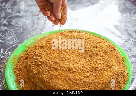 Kochen hausgemachten Kuchen. Eine Frau streut einen gebackenen und cremefarbenen Kuchen mit Süßwarenbröseln. Stockfoto