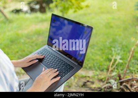 Nahaufnahme einer Frau, die im Garten auf der Laptop-Tastatur arbeitet und tippt Stockfoto