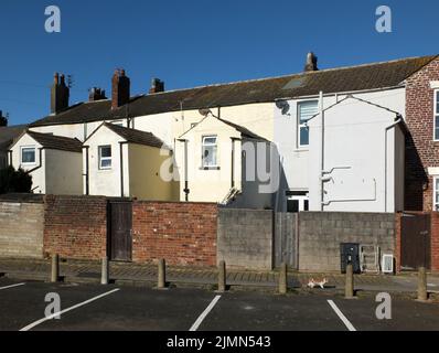 Blick auf die Rückseite einer Reihe von weiß-gelb gestrichenen typischen kleinen englischen Reihenhäusern mit Parkplätzen in fleetwood lan Stockfoto