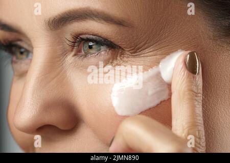Frau mittleren Alters, die Anti-Aging-Creme auf ihr Gesicht auftragen Stockfoto