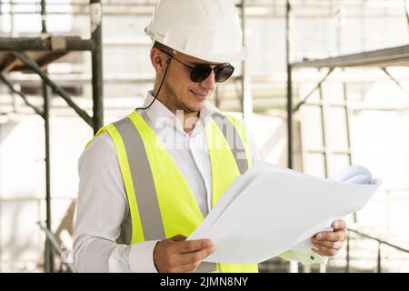 Mann Architekt trägt Sicherheitsweste mit einem Bauplan auf einer Baustelle Stockfoto