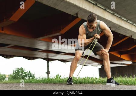 Muskulöser Mann beim Training mit einem Widerstand Gummibänder auf einer Strecke Stockfoto