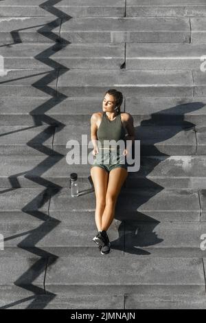 Sportliche Frau, die nach dem Fitness- oder Joggingtraining auf einer Treppe sitzt Stockfoto