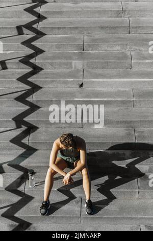 Selbstbewusste sportliche Frau, die nach dem Fitness- oder Joggingtraining auf einer Treppe sitzt Stockfoto