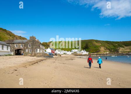 Paar zu Fuß in Porthdinllaen bei Morfa Nefyn an der Küste von Nord-Wales. Das bekannte Ty Coch Inn zwischen den weiß getünchten Hütten. Stockfoto