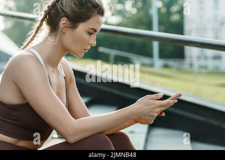 Eine athletische Frau, die während ihres Fitness-Trainings im Freien ihr Smartphone benutzt Stockfoto