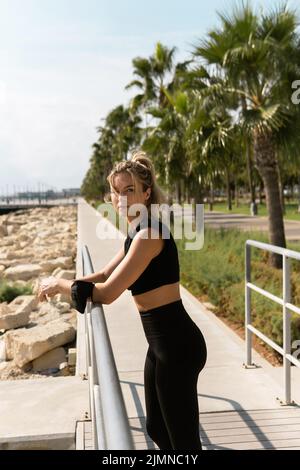 Eine athletische Frau mit einer Gesichtsmaske auf ihrem Unterarm entspannt sich nach dem sommerlichen Street Workout Stockfoto