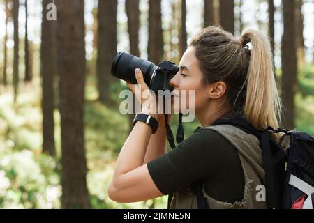 Wanderer, der mit einer modernen spiegellosen Kamera im grünen Wald fotografiert Stockfoto