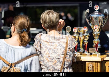 07. August 2022, Hessen, Fulda: Besucher sitzen an einem Tisch neben den Siegertrophäen der vergangenen Jahre. Am 06. Und 07. August 2022 fand in Fulda die Deutsche Grill- und BBQ-Meisterschaft 25. statt. Profis und Amateuren kämpften um den Sieg. Die Branche präsentierte sich mit verschiedenen Ständen und Veranstaltungen. Foto: Hannes P. Albert/dpa Stockfoto