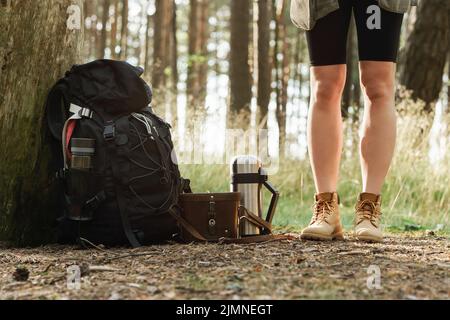 Weibliche Beine und Wanderrucksack auf dem Boden Stockfoto