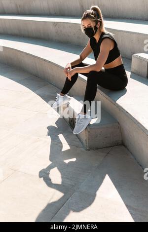 Athletische Frau trägt Gesichtsmaske während des sommerlichen Straßentrainings Stockfoto