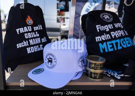 07. August 2022, Hessen, Fulda: "Frau mit Grill sucht Mann mit Holzkohle" steht auf einem T-Shirt, das an einem Stand mit Merchandise-Produkten des deutschen Metzgerhandwerks bei der Deutschen Grill- und BBQ-Meisterschaft 25. ausgestellt ist. Die Meisterschaft fand vom 6. Bis 7. August 2022 in Fulda, Deutschland, statt. Profis und Amateuren wetteiferten um den Sieg. Die Branche präsentierte sich mit verschiedenen Ständen und Veranstaltungen. Foto: Hannes P. Albert/dpa Stockfoto