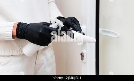 Hände mit Handschuhen, die den Türgriff desinfizieren Stockfoto