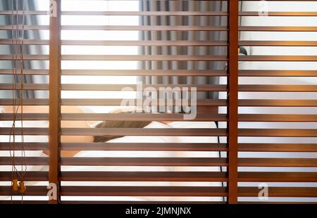 Hölzerne Jalousien. Verdunkelungsvorhang zwischen Bad und Schlafzimmer im Hotel mit Blick auf die Frau schlafen unter weißen Decke auf dem Bett am Morgen Stockfoto