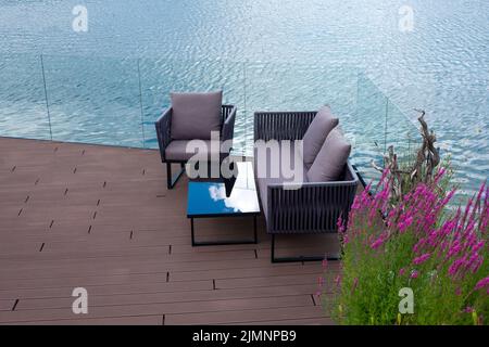 Bequeme Sofas und ein Tisch auf einer Holzterrasse am Wasser. Ein schöner Ort zum Entspannen auf dem Teich. Erholungs- und Entspannungsbereich. Stockfoto