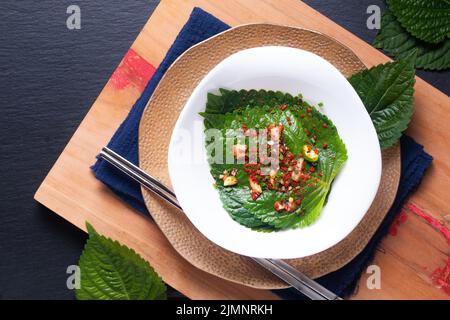 Asiatisches Lebensmittelkonzept hausgemachte koreanische Bio-Kkaennip Kimchi, Perilla(Shiso) Kimchi in weißer Keramikschale auf Holzbrett mit Kopierfläche Stockfoto