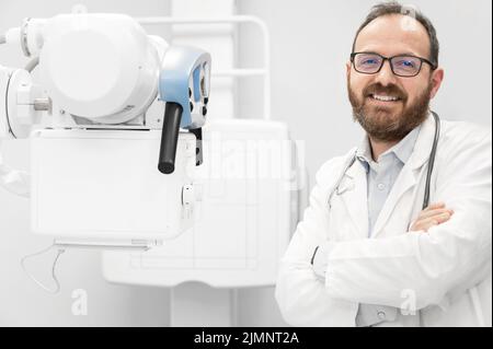 Lächelnder, selbstbewusster Radiologe, der in der Nähe von Röntgengeräten steht. Stockfoto