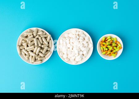 Türkisfarbener Hintergrund einer großen Gruppe von verschiedenen Kapseln, Pillen und Tabletten in weißen Schalen in einer Reihe Stockfoto