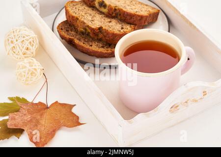 Herbstliche Essensscheiben Bananenbrot, eine Tasse Tee, trockene Blätter, weißer Holztisch. Gemütliches Zuhause Winter. Seitenansicht, Kopierbereich Stockfoto