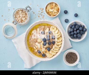 Haferflocken mit Heidelbeeren, Banane auf blauem Hintergrund. Draufsicht. Gesundes Frühstück Stockfoto