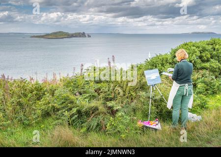 Frau malt auf Leinwand Irlands Eye Island, während sie draußen auf dem Howth Cliff Walk ist Stockfoto