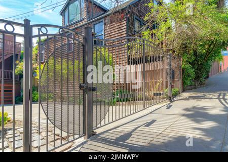 Schmiedeeisernes schwarzes Tor einer Residenz in San Francisco, Kalifornien. Vorderseite eines Hauses mit Betoneinfahrt und Blick auf einen Baum in der Nähe des Hauses mit Stockfoto